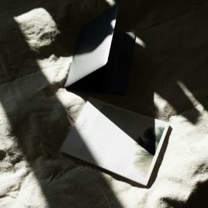 From above of opened laptop and book placed together on soft blanket on bed in light bedroom in daylight